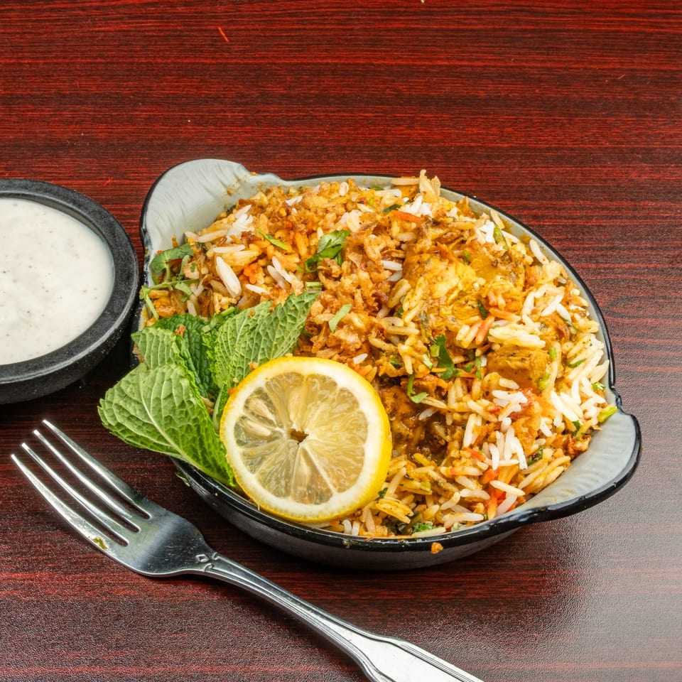 Bombay Cafe's chicken biryani with mint, lemon, and a side of raita on a wooden table.