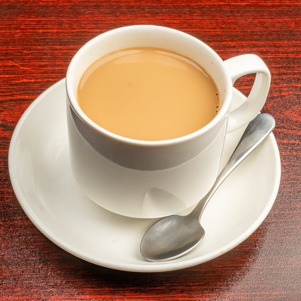 A white cup of Indian chai tea with a spoon on a saucer, on a dark red table.