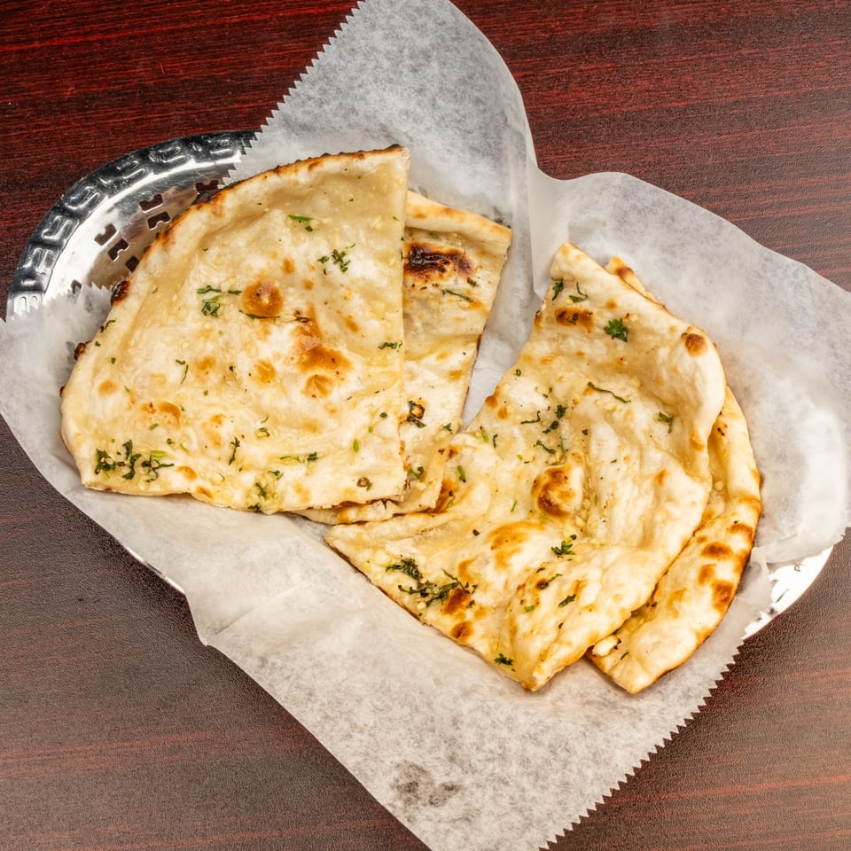 Freshly baked Indian naan bread, garnished with herbs, served in a metal basket lined with parchment paper.
