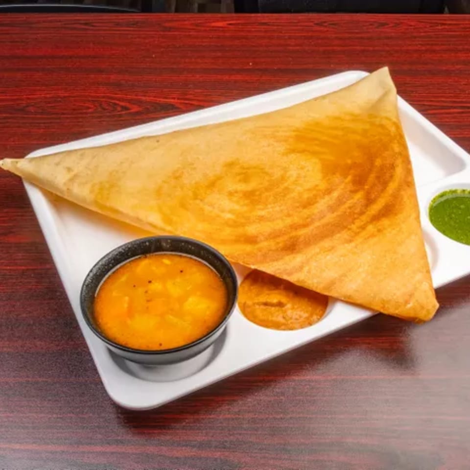Golden brown dosa, a thin Indian pancake, served with two chutneys and sambar on a white plate.