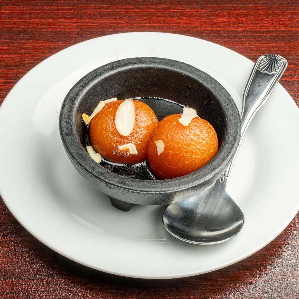 Two gulab jamun, Indian fried dough balls, in a black bowl with syrup and almond slivers.