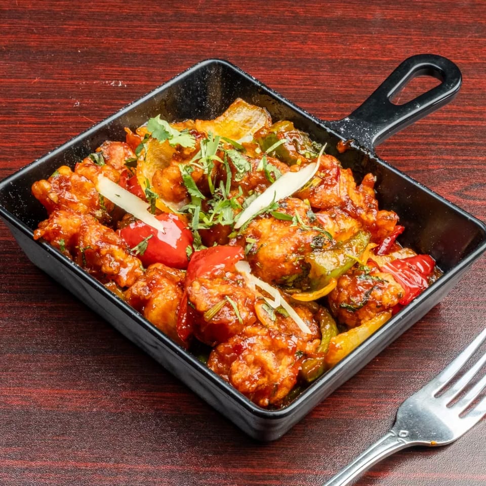 Bombay Cafe's Indian chili chicken, garnished with cilantro and ginger, served in a black skillet.